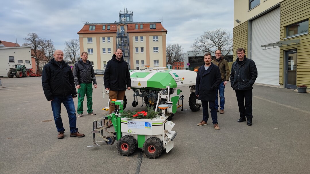 Coronakonforme und dennoch feierliche Übergabe des Dino in Köllitsch, Sachsen: Den „Schlüssel“ zur Fern-Bedienung des Roboters überbrachte Dinos kleiner Bruder „Oz“ (im Vordergrund). V. li. n. re.: Frank Nicklisch, BayWa Verkaufsberater Sachsen; Marvin Wenzel, Servicetechniker Smart Farming für Sachsen; Cornelius Donath, Verkaufsleiter Europa Naio Technologies; Till Kunkel, Projektmitarbeiter Landnetz; Dr. Maximilian Deutsch, Leiter Stabstelle Digitalisierung beim LfULG; Dr. Uwe Bergfeld, Abteilungsleiter Landwirtschaft beim LfULG.