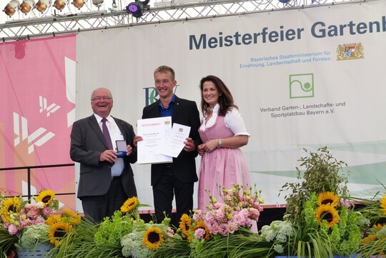 Jonas Engelhardt (Mitte) aus Frth bekommt als bester Absolvent 2018 im Gemsebau neben seinem Meisterbrief den Meisterpreis der Bayerischen Staatsregie-rung berreicht. Mit ihm freuen sich Roland Albert (Prsident des Bayerischen Grtnerei-Verbandes) und die bayerische Landwirtschaftsministerin Michaela Kaniber.
